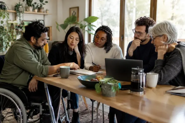 Diverse adult community group reviewing shared meeting notes around an accessible table.